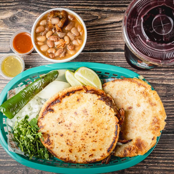 Taquitos Don Agaves tacos with beans, sauces, lime, cilantro, onion, and a drink on a wooden table.