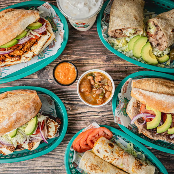 Overhead view of Taquitos Don Agaves burritos, tortas, beans, and salsa on a wooden table.