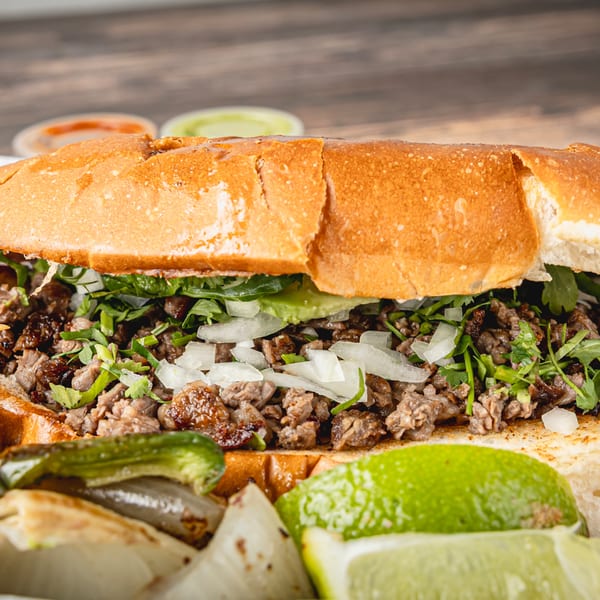 A close-up of a Taquitos Don Agaves torta filled with meat, onions, cilantro, and avocado.