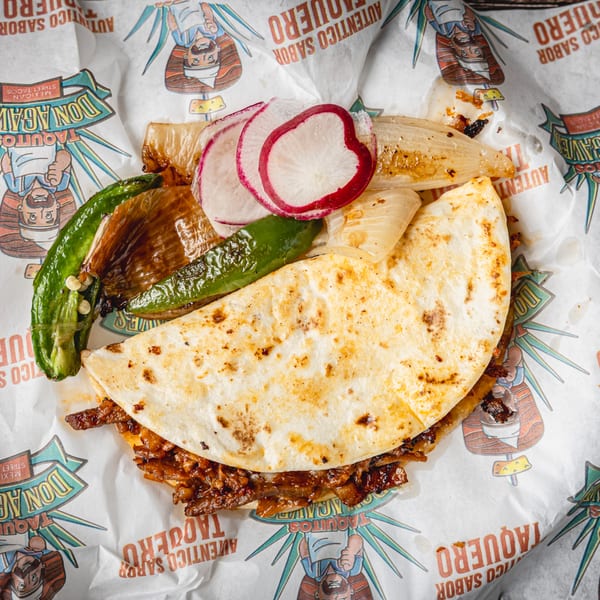 A Don Agaves taco with grilled onions, jalapeños, and radish slices on branded paper.