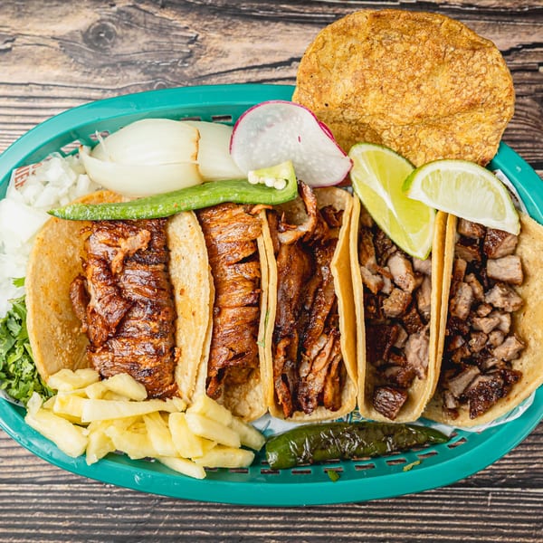 A vibrant platter of Taquitos Don Agaves tacos with various meats, limes, onions, radishes, and peppers.